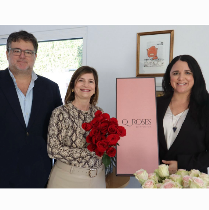 Os sócios fundadores da QRoses, um homem e duas mulheres, a posar para a câmara com um ramo de rosas vermelhas.